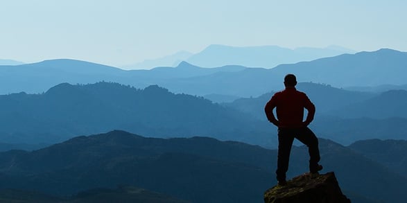 A man stands on a mountaintop with his hands on his hips